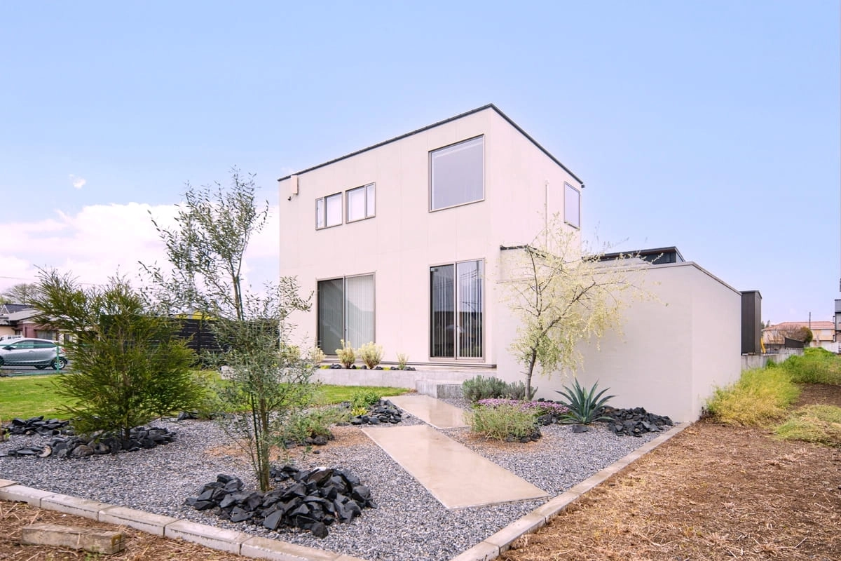 砂利敷きの前庭と植栽がある白い箱型の2階建て住宅