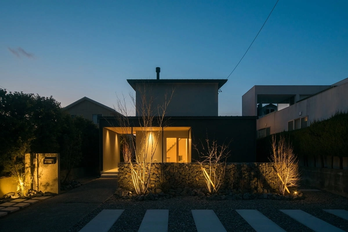 ライトアップされた植栽と石積みの壁があるモダンな住宅