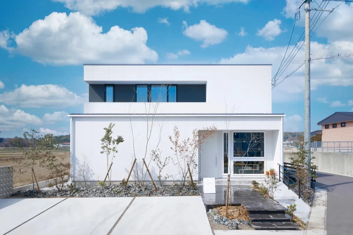 アプローチの植栽と青空が映える白い箱型の2階建て住宅