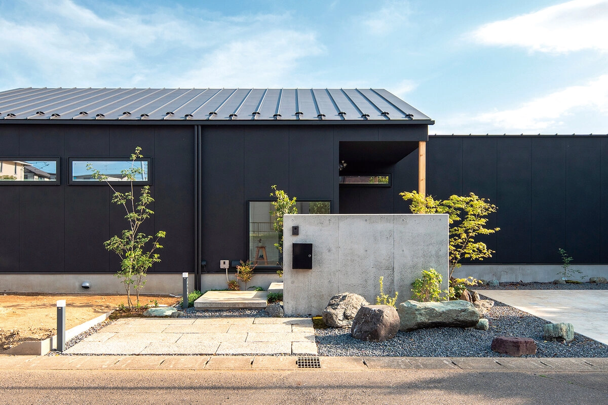 黒い外壁に打ち放しコンクリートの門柱が映える平屋の外観