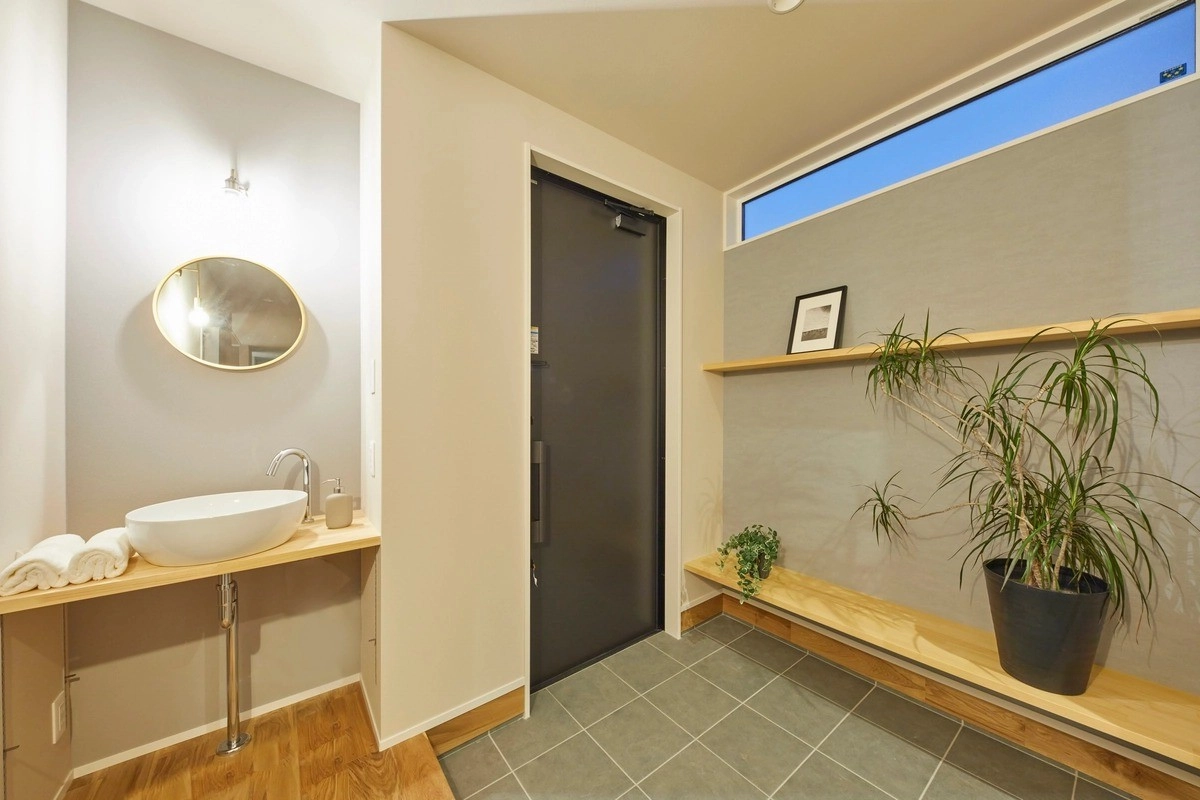 グレーの壁に映える白い洗面ボウルと観葉植物のある玄関