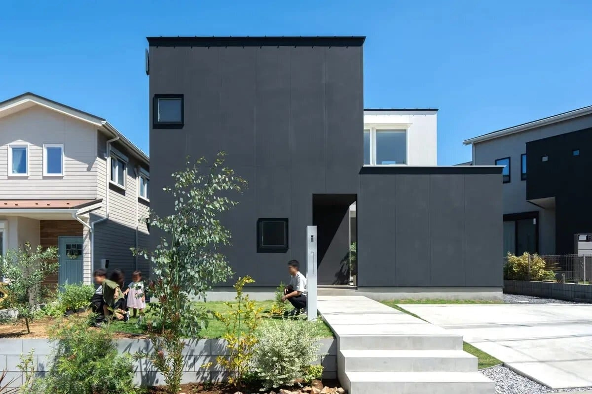芝生の庭で遊ぶ家族と黒い箱型のモダンな住宅