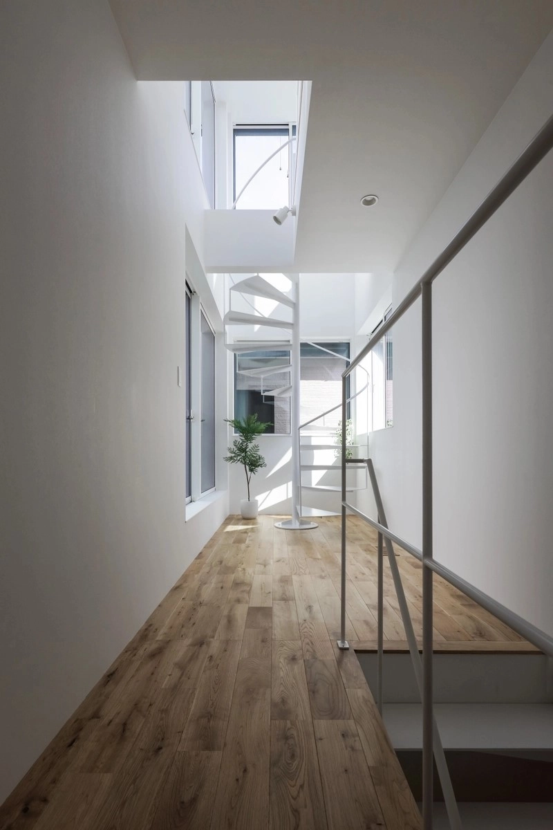 白い壁と明るい床材の空間に繊細なデザインの白い螺旋階段がアクセントとなる吹き抜けの廊下