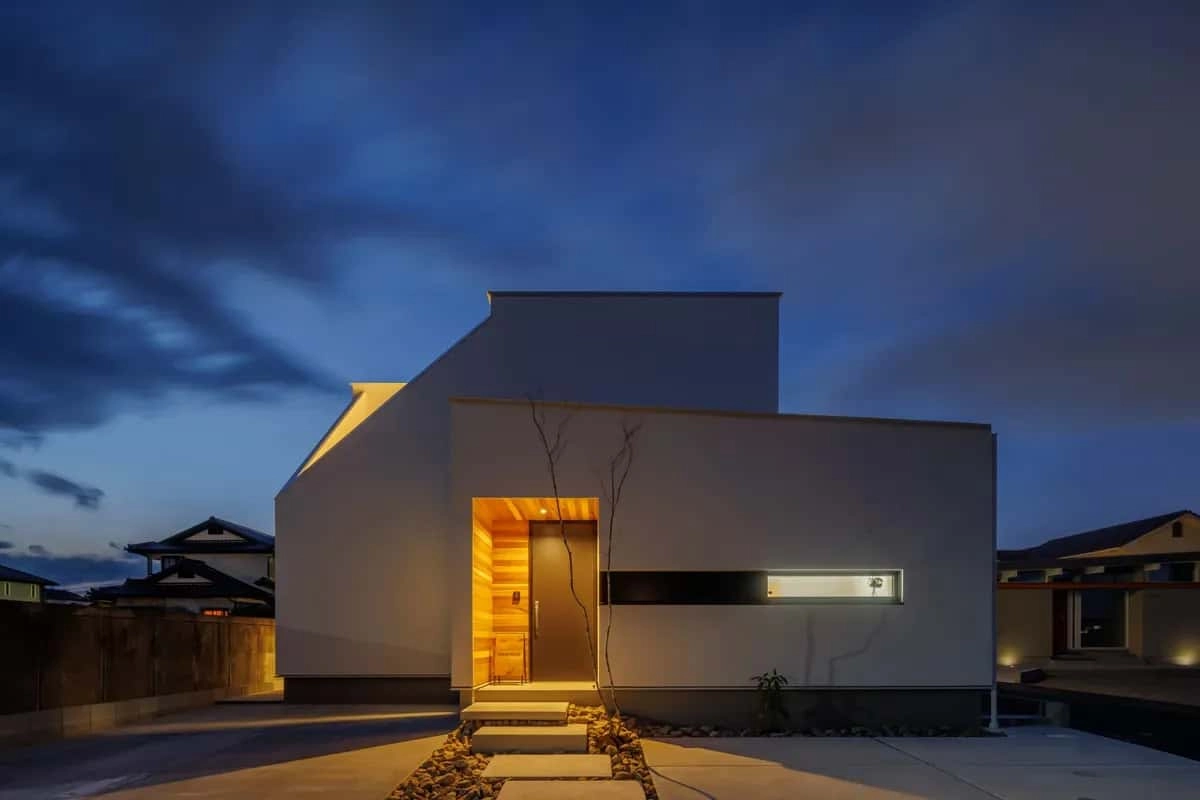 ライトアップされた板張りの玄関が際立つ白い住宅の夕景