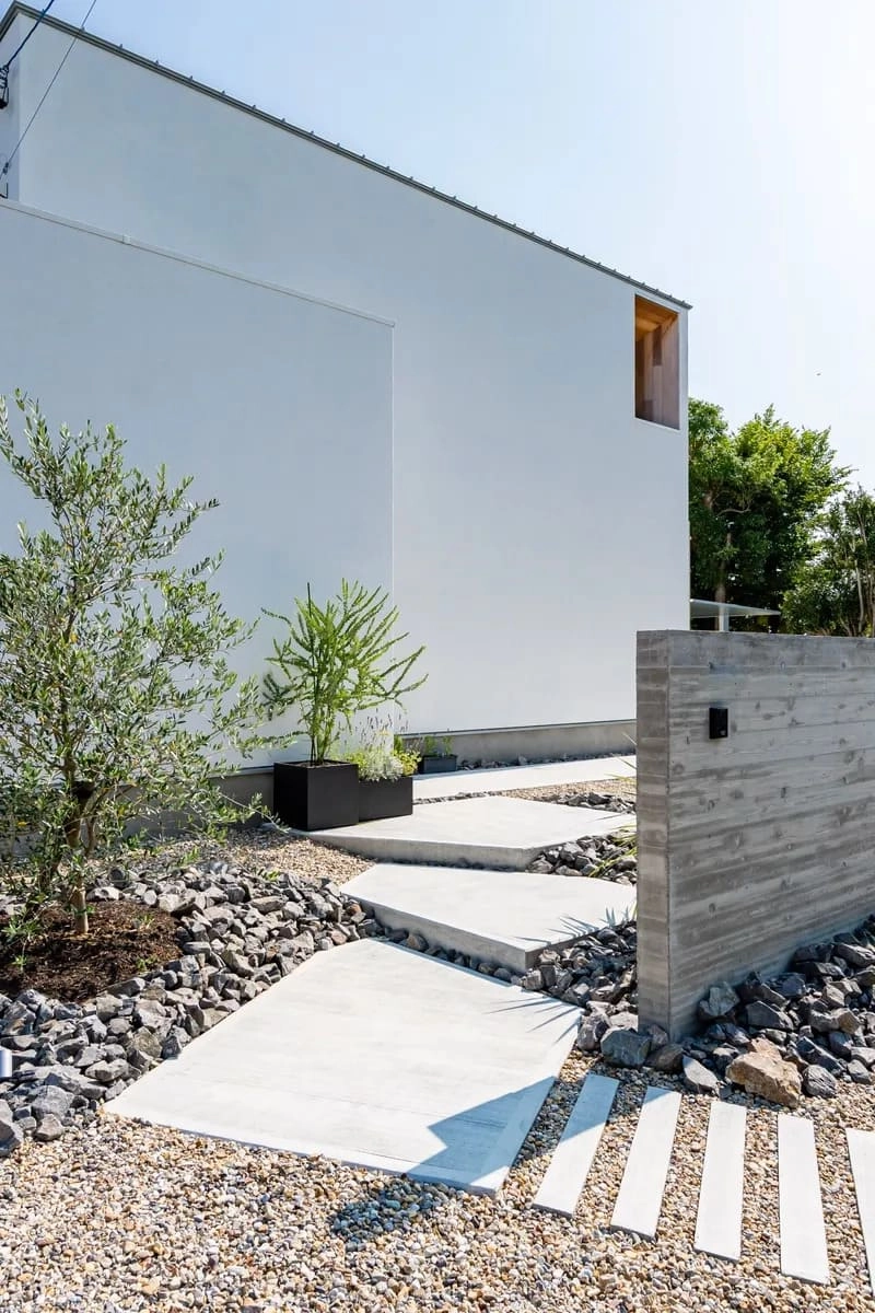 コンクリート壁と石敷きのアプローチがある白い住宅