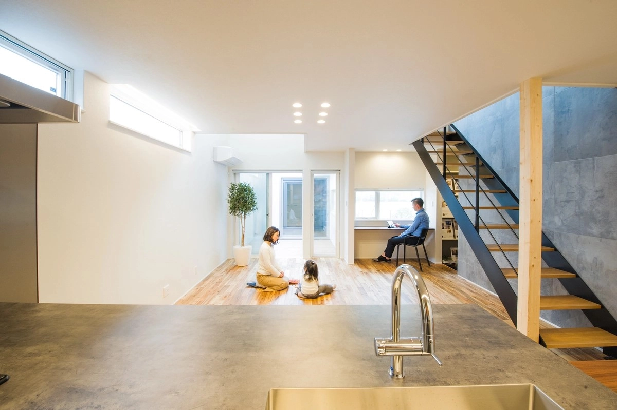 吹き抜けのリビングで遊ぶ親子とデスクワークをする男性が共存する明るいLDK