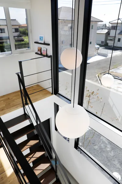 風景と重なる大きな窓の家の吹き抜け・階段・照明